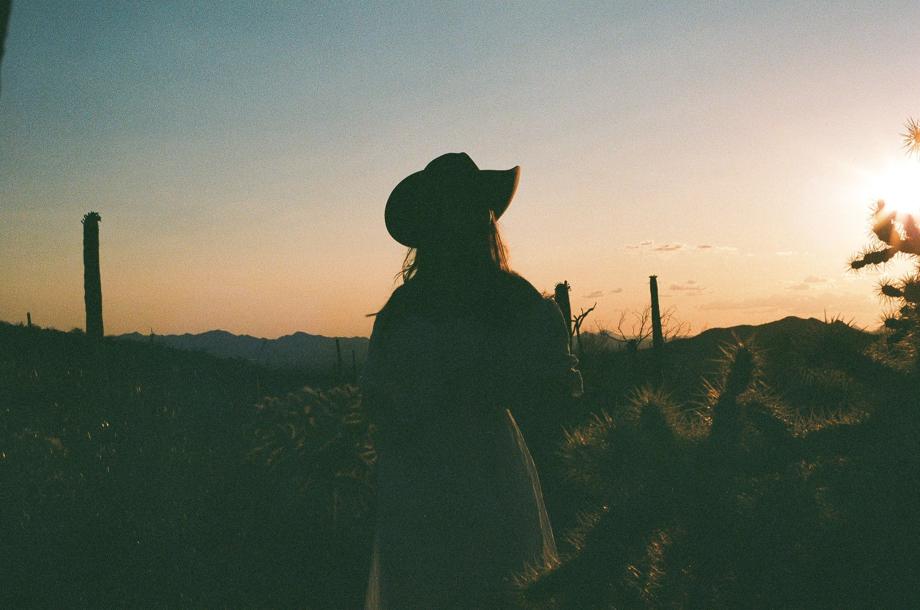 Woman standing in the desert during sunset. Woman is wearing a cowboy hat