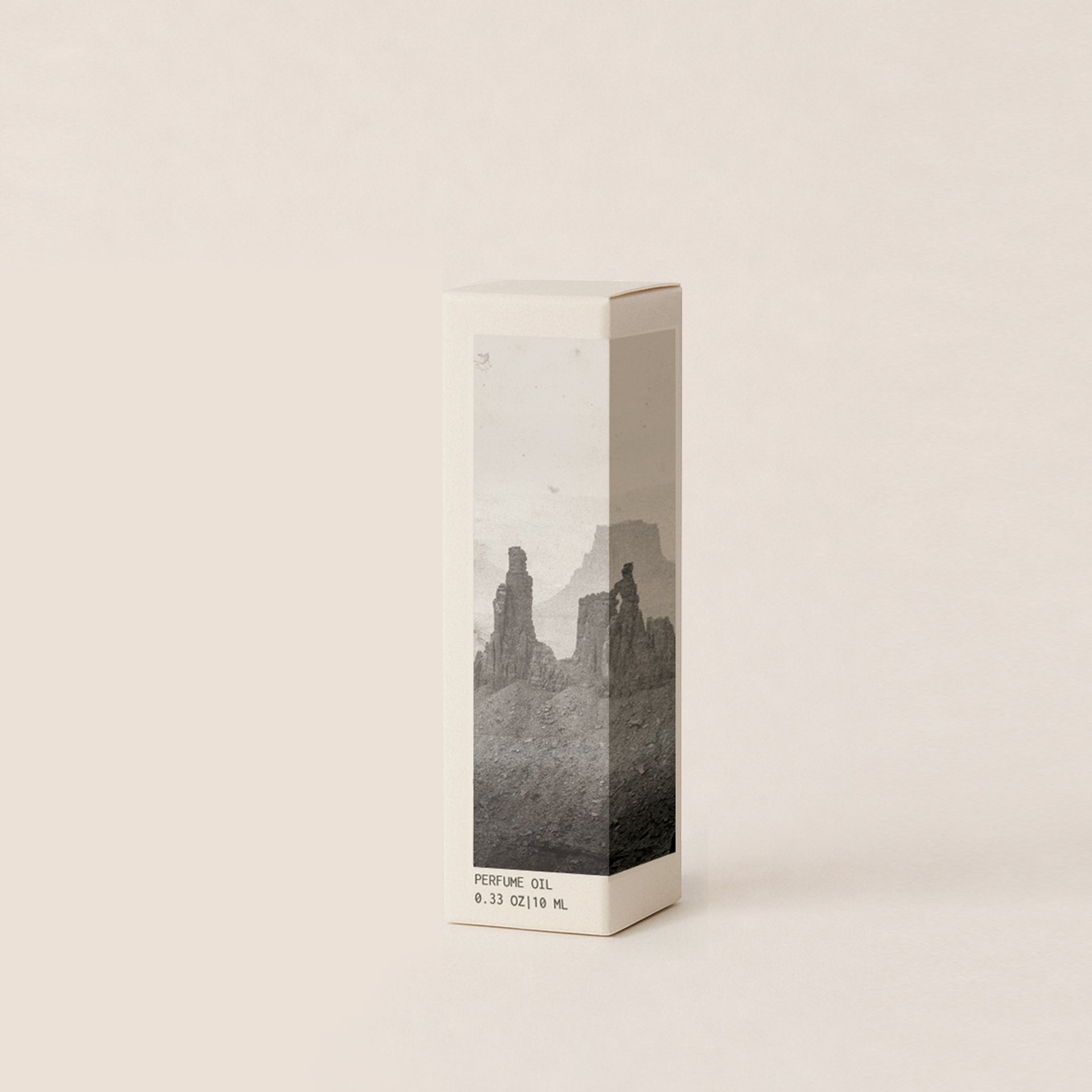 A tall rectangular box of perfume oil with a minimalist black and white landscape photograph on the front, standing on a light beige background.