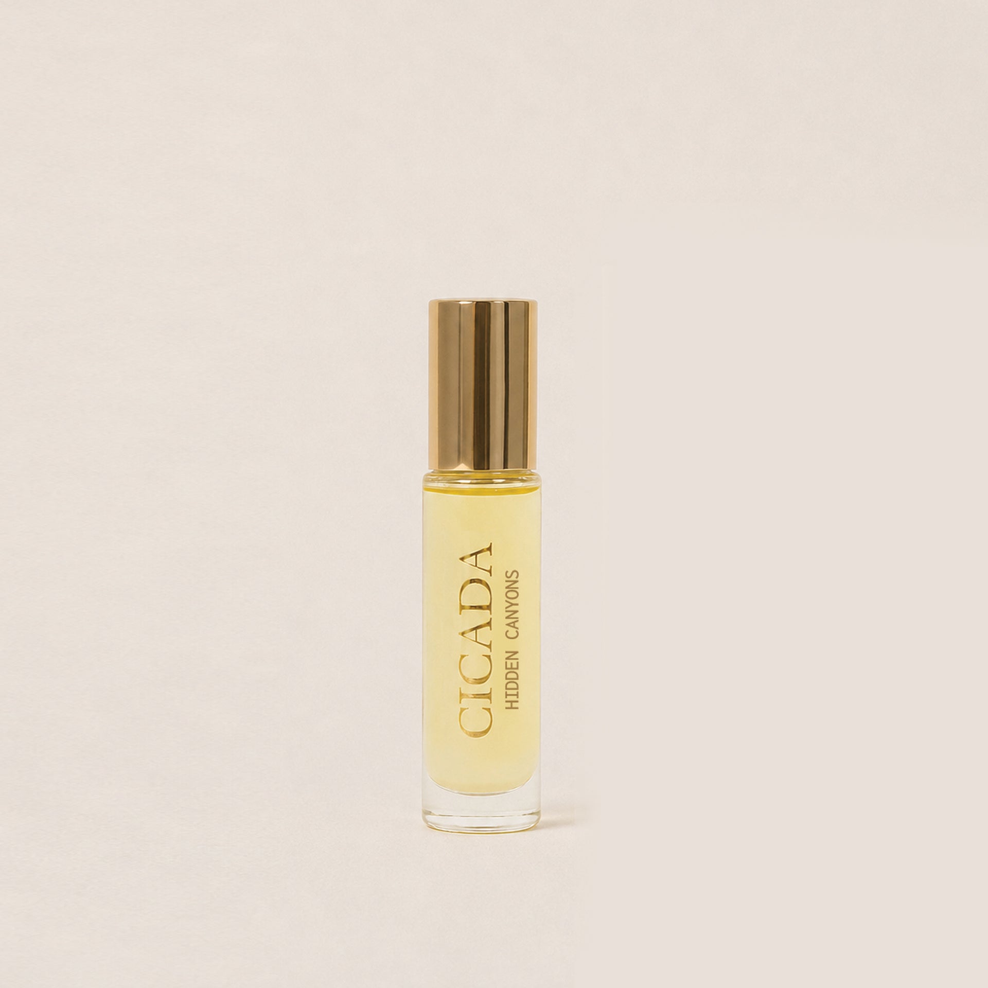 A small cylindrical glass bottle of Cicada Hidden Cactus fragrance oil with a metallic gold cap, set against a solid, warm off-white background.