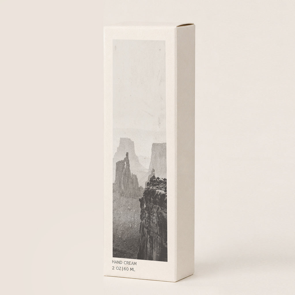 A tall, cream hand cream box with a black-and-white canyon landscape print on the front, photographed against a plain warm off-white background. 