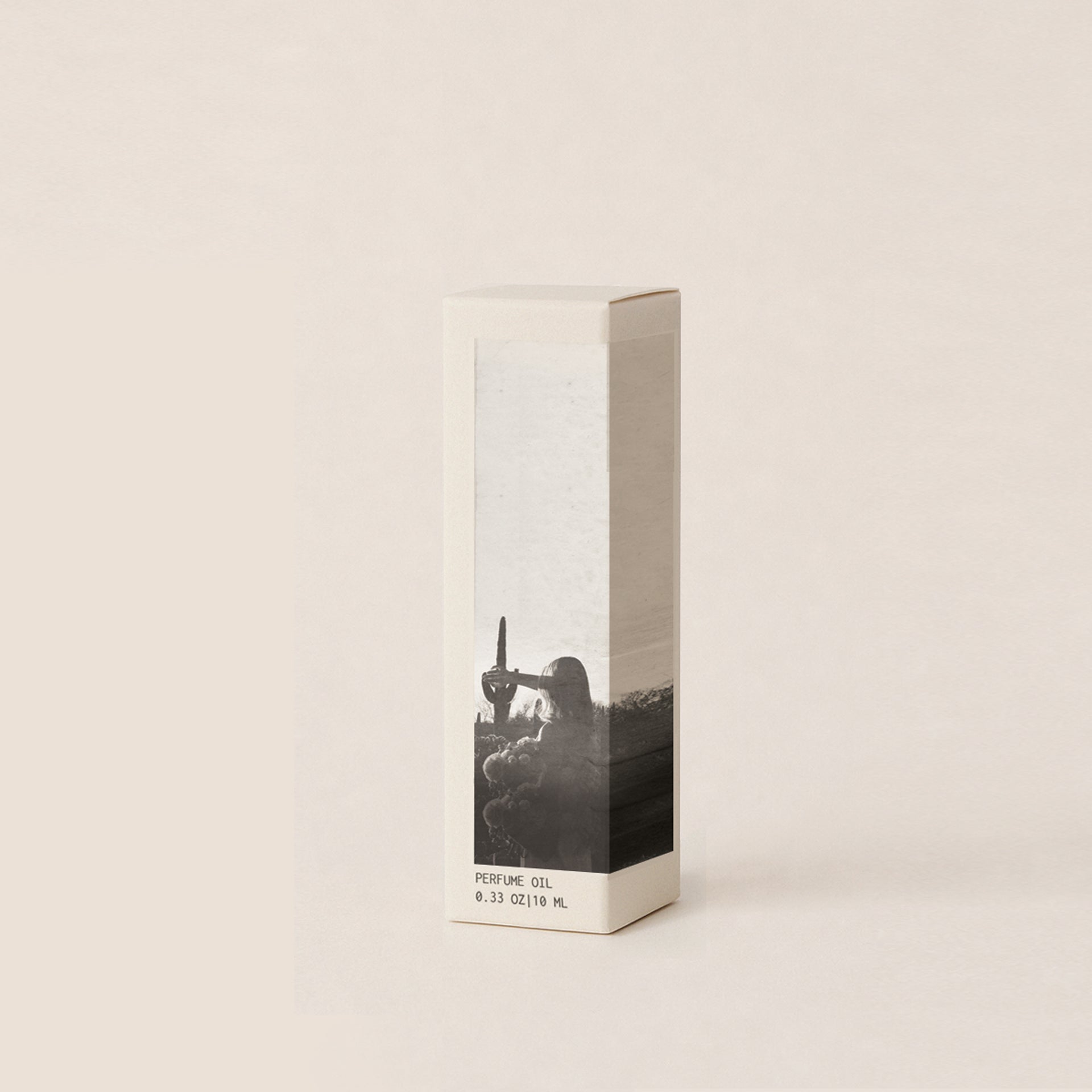 A tall, narrow rectangular perfume box with a minimalist design, featuring a black and white photographic print of a woman and cactus landscape on a light beige background, set against a solid cream backdrop.