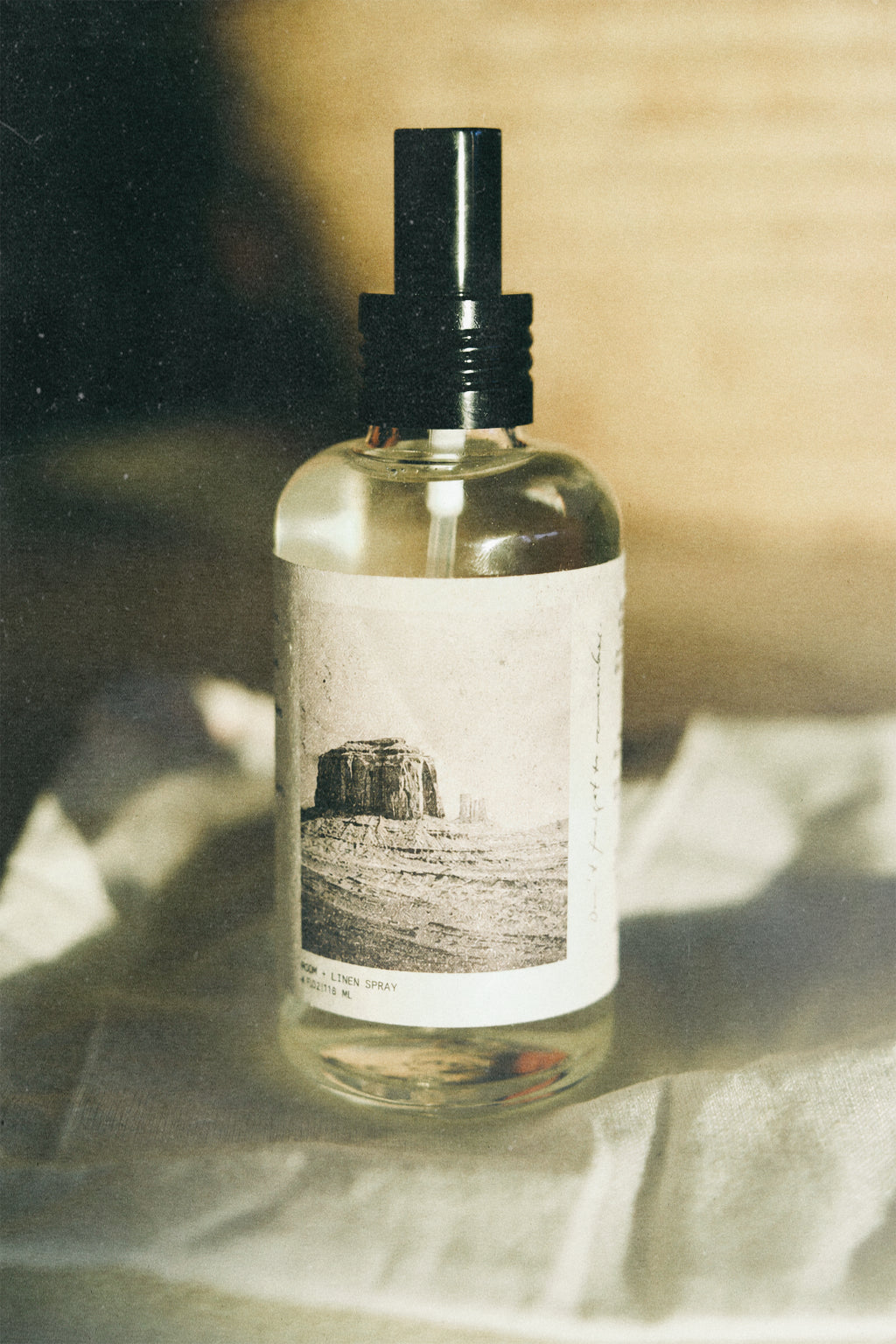 Image of a glass atmosphere spray bottle with black cap and image of plateau on it. 