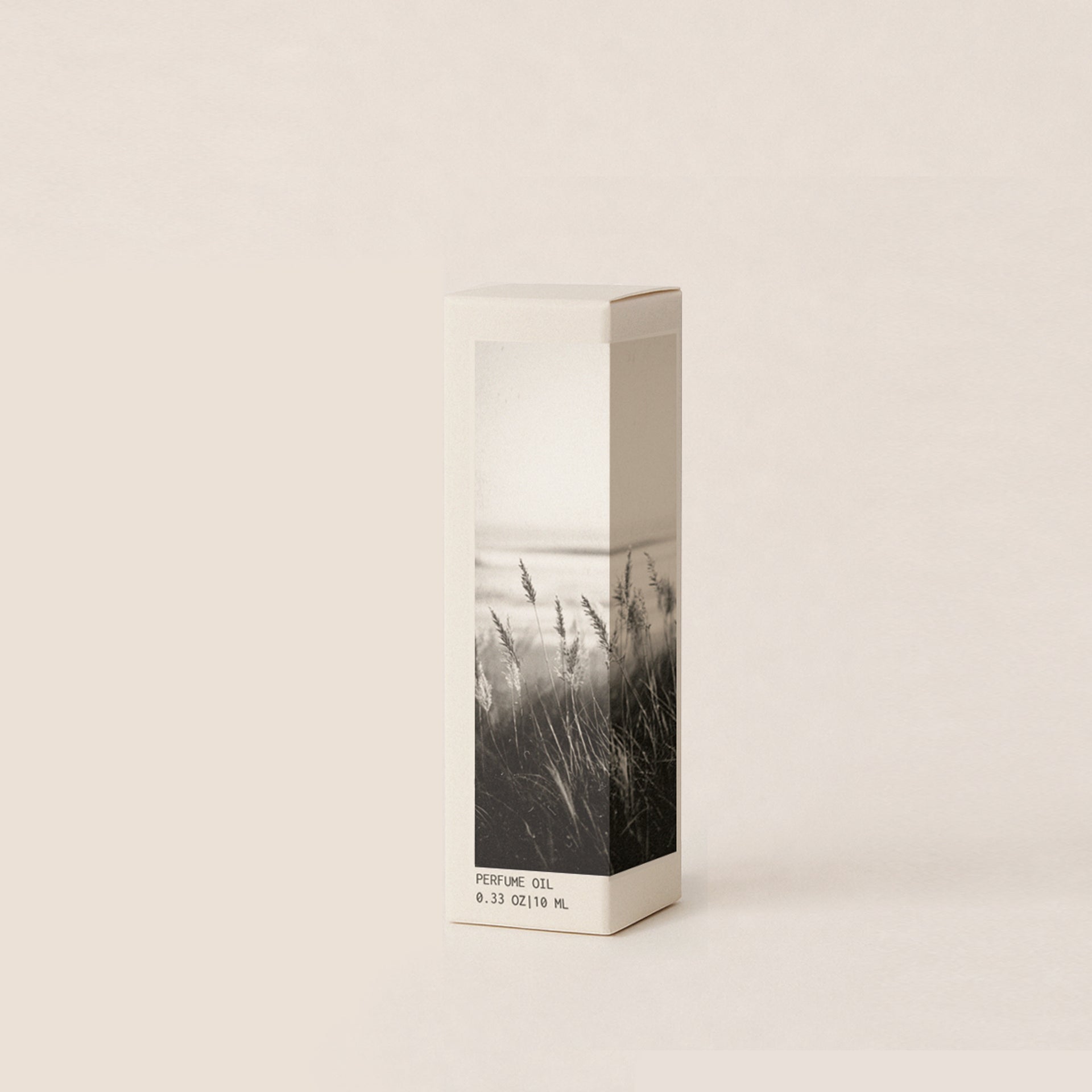 A cream colored rectangular perfume oil box with a minimalist black and white photograph of beach grass, standing on a light beige background.