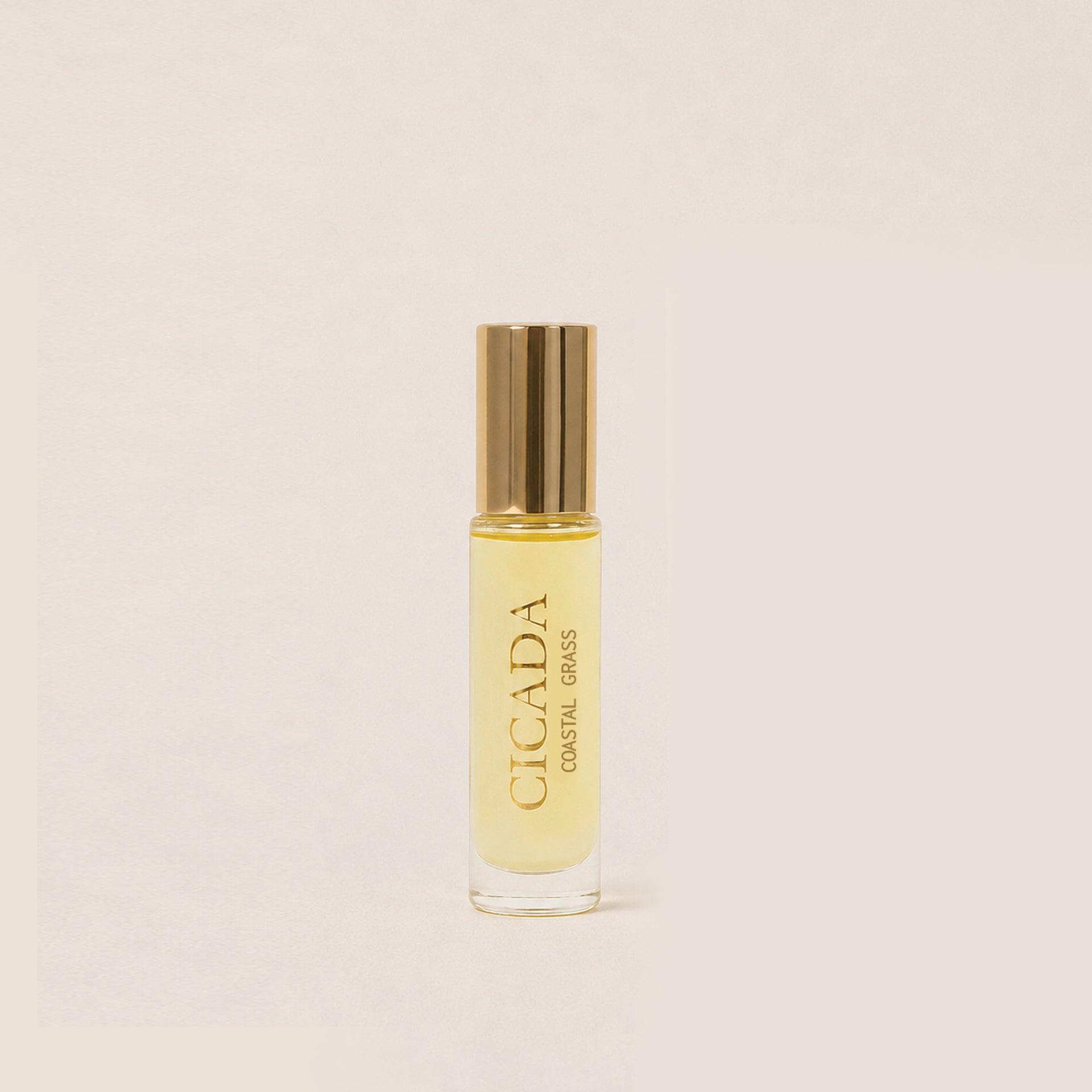 A small clear glass bottle of Cicada Coastal Grass roll-on perfume oil with a shiny gold cap, set against a solid light beige background.