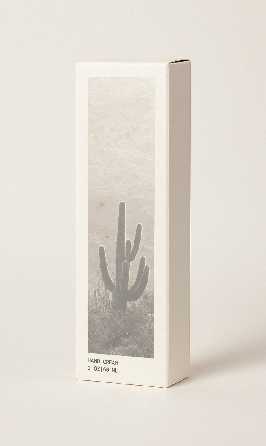 Product image of CICADA hand cream box that hand cream comes in. Box measures 2" wide x 1.25" deep x 6.5" high. Box is light cream with black and white cactus and desert landscape image on it. Box also has the text 'Hand cream' and product weight of '2 oz | 60 ml'. Image has a cream colored background. 