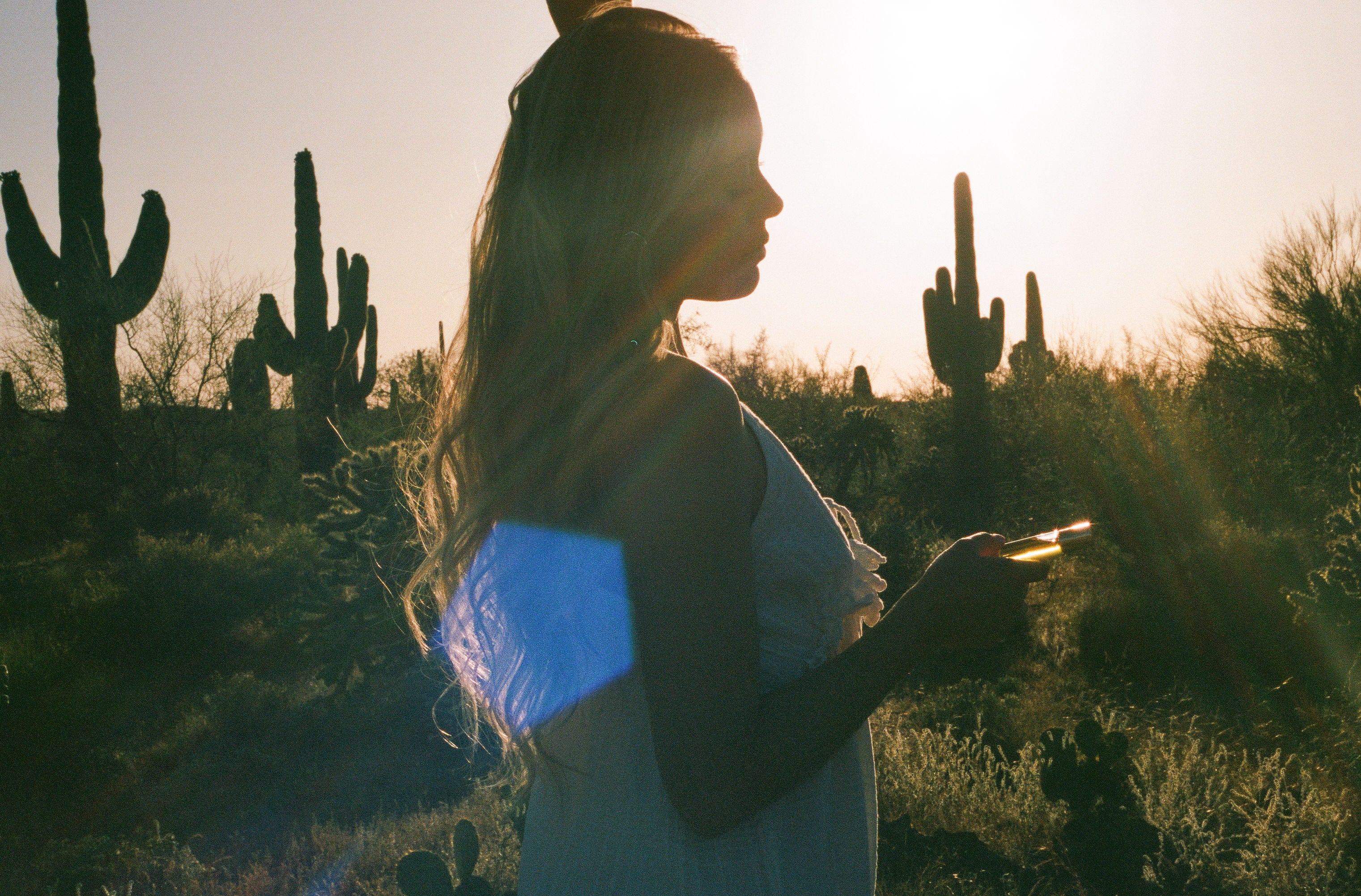 Lifestyle image of woman standing in the desert holding CICADA perfume oil. 