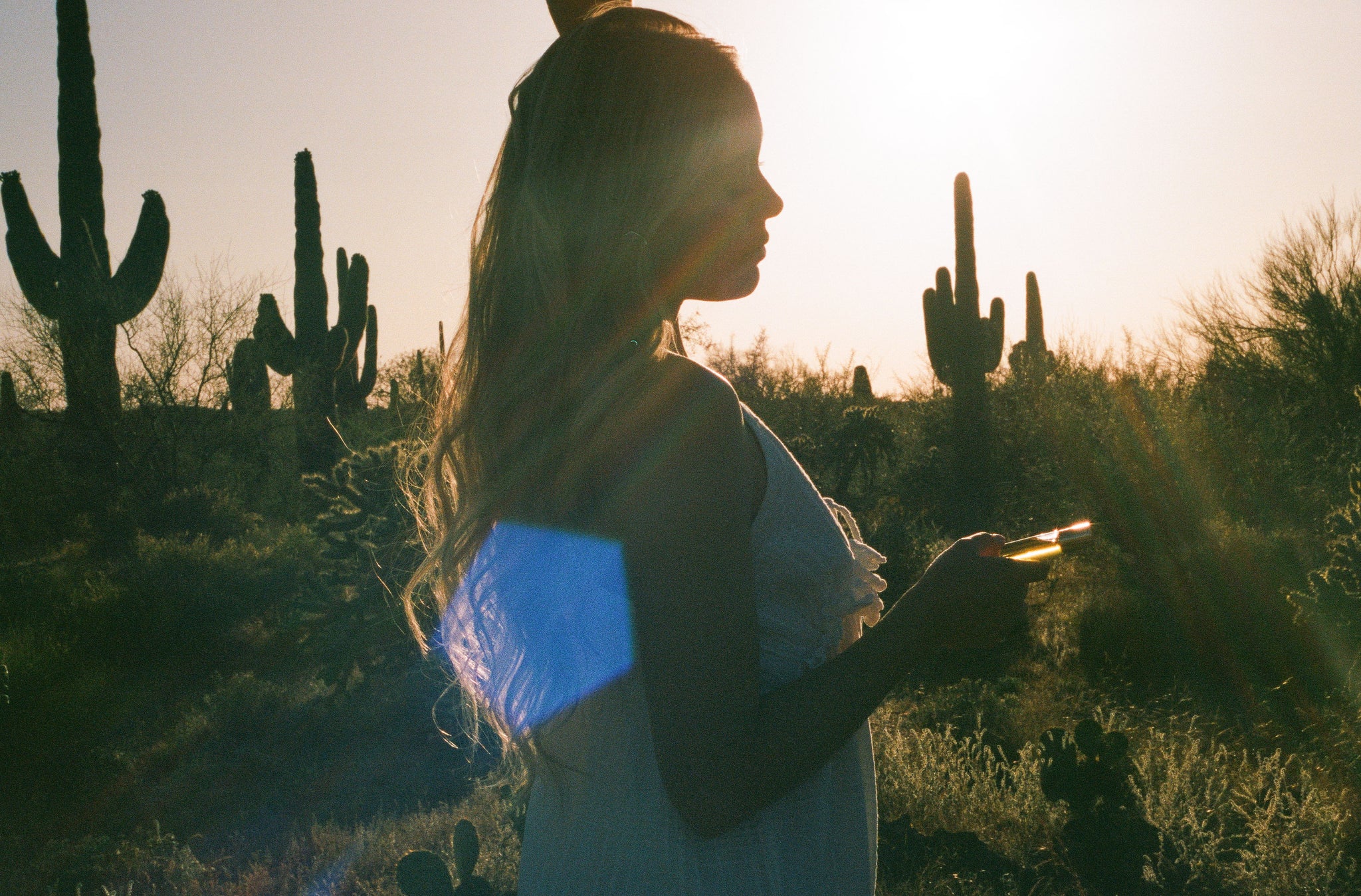 Lifestyle image of woman standing in the desert holding CICADA perfume oil.