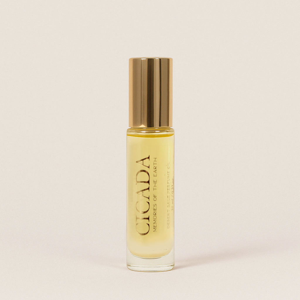 Product image of CICADA glass roller bottle of perfume oil with gold cap, labeled with the brand name and scent description. Background of image is cream colored. 