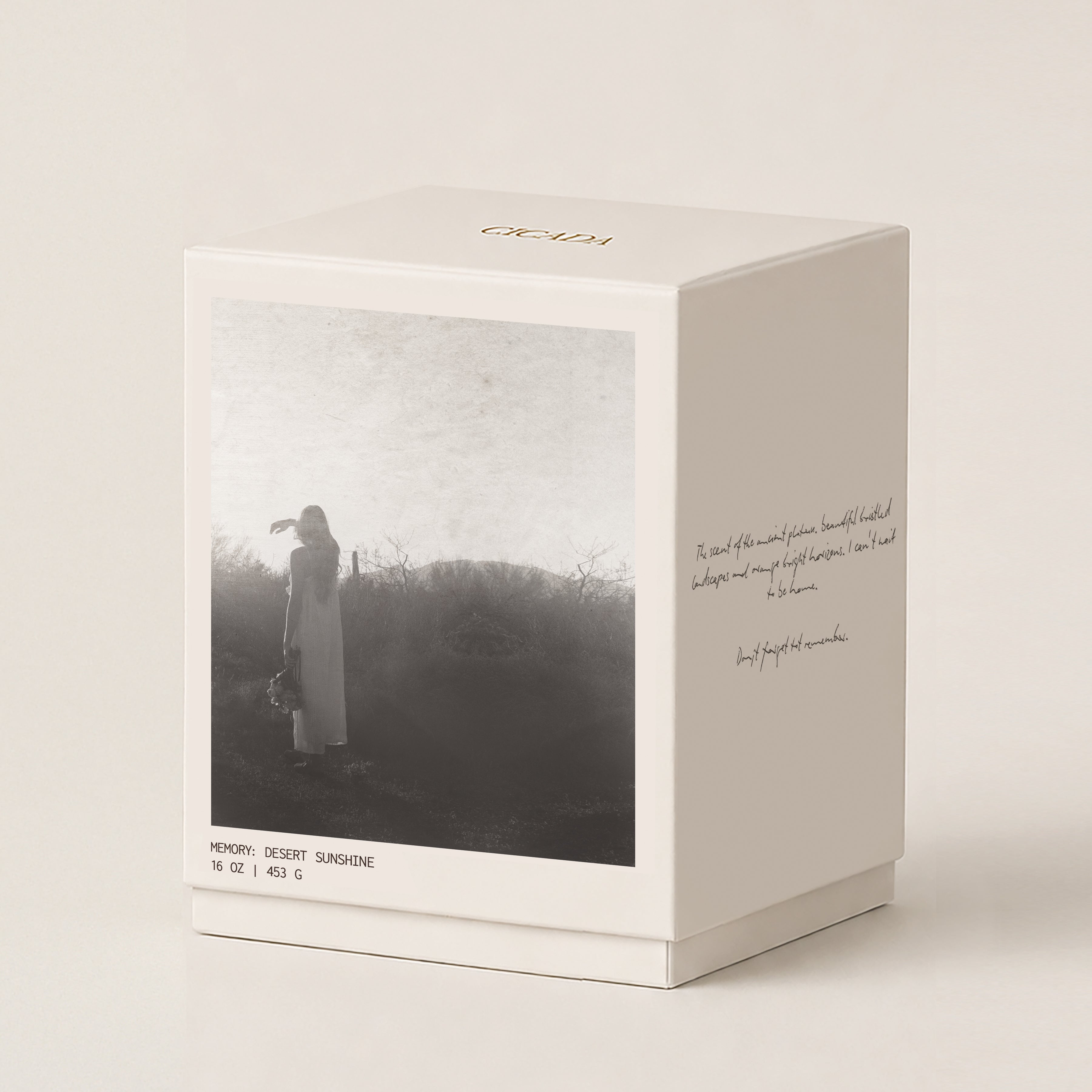 A cream 16 oz candle box with a printed black-and-white photo of a woman standing outdoors, handwritten-type script on the side, and the brand name CICADA printed in gold at the top, shown on a warm off-white background.