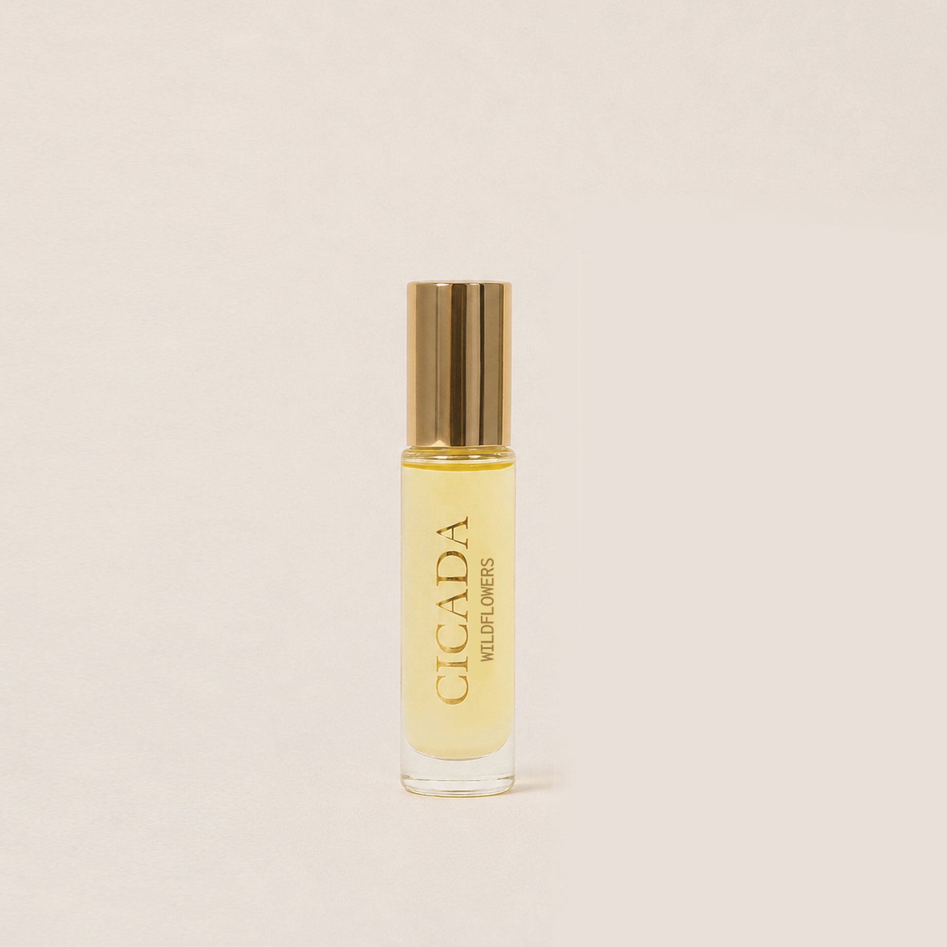 A small cylindrical glass bottle of Cicada Wildflower roll-on perfume oil with a metallic gold cap, set against a solid light beige background.